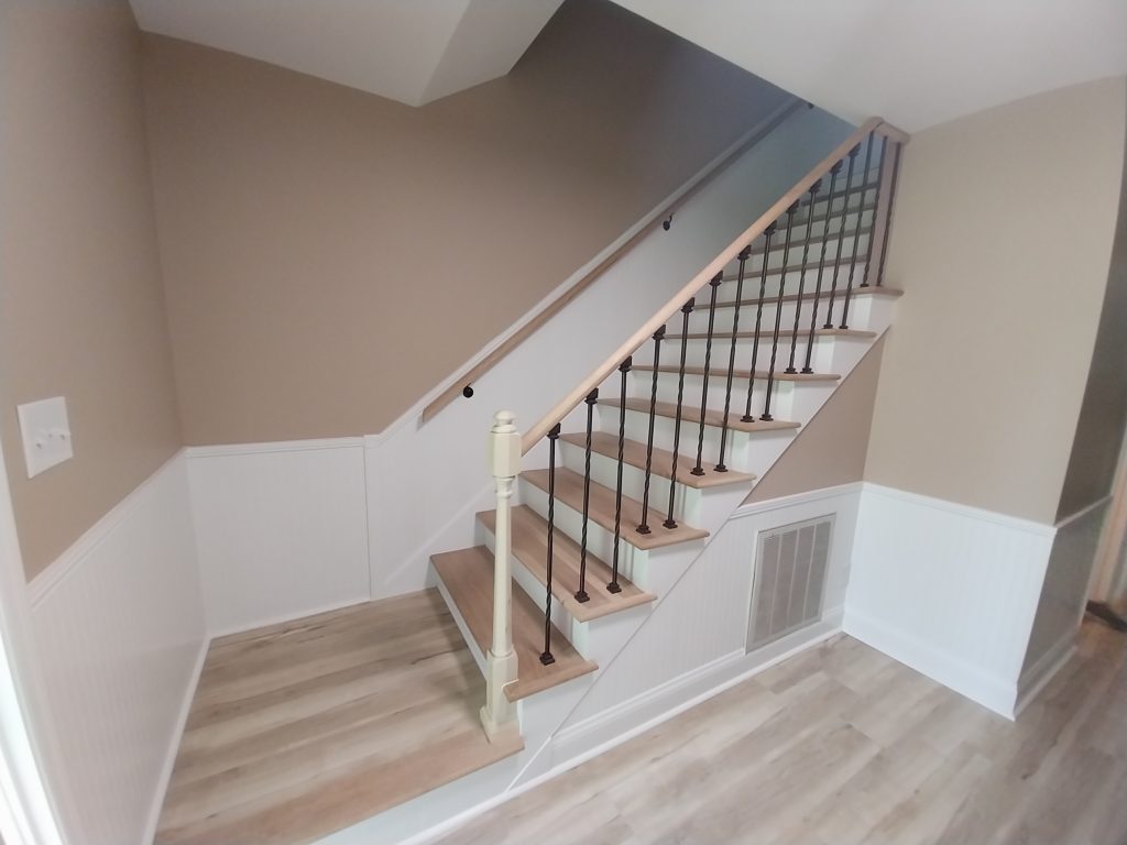 Custom residential staircase featuring hardwood treads, black metal balustrade, and wainscoting installation by Aiken general contractor.