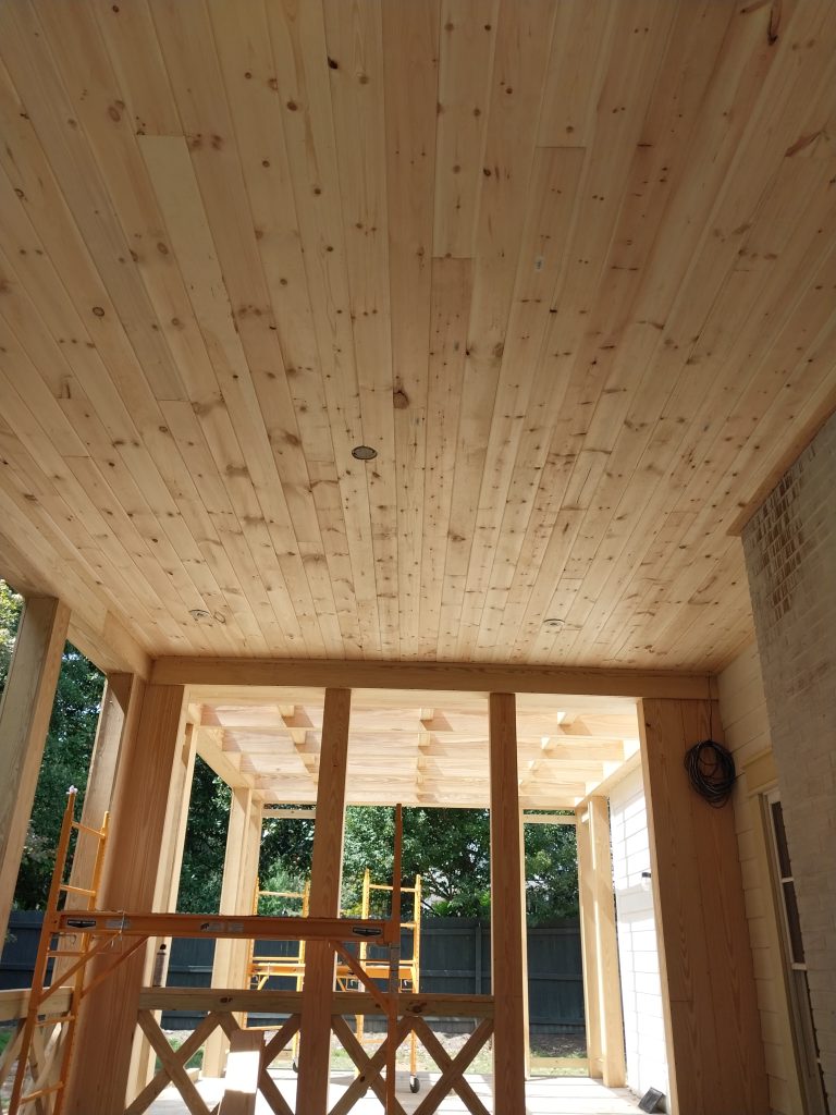 Modern residential construction featuring light pine wood paneling, large timber-frame windows, and natural finishes in a cabin-style home addition.