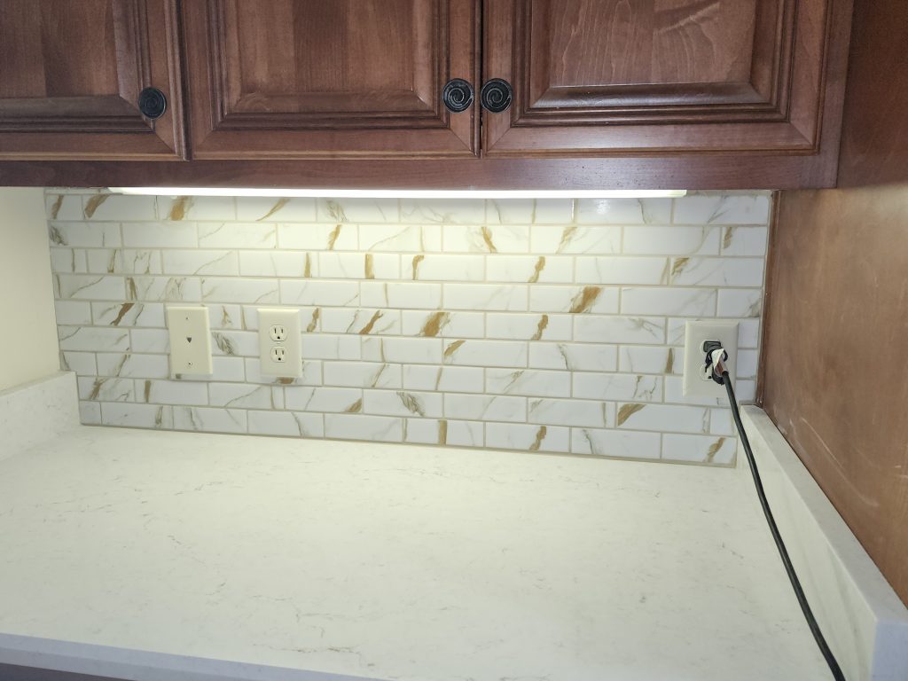 Professional tile installation of marble subway backsplash above quartz countertop in residential kitchen remodel.