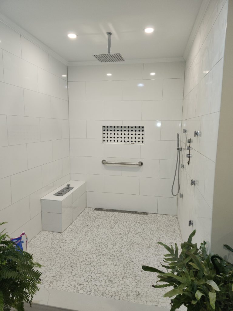 Modern shower enclosure with subway tile walls, frameless glass door, rainfall showerhead, and mosaic accent panel installed by professional tile contractor.
