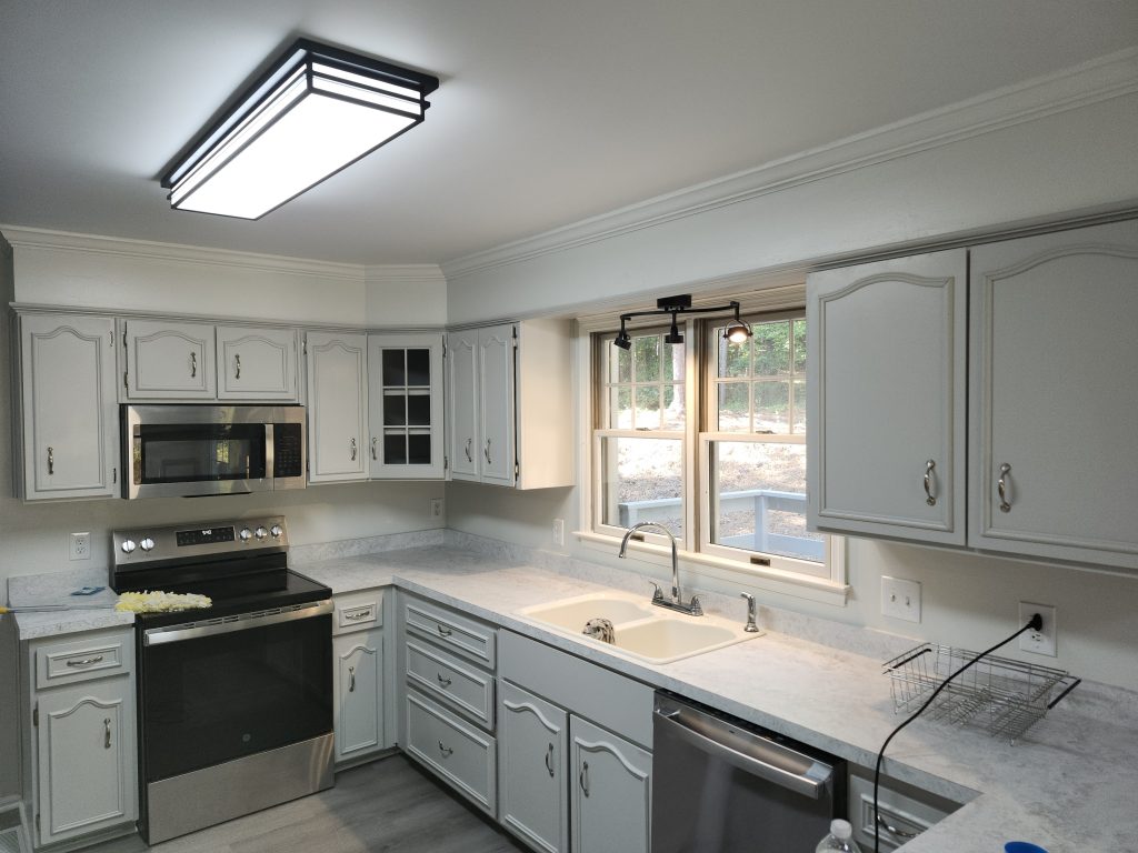 Modern L-shaped kitchen renovation featuring white cabinetry, marble countertops, and stainless steel appliances with professional finishing touches.