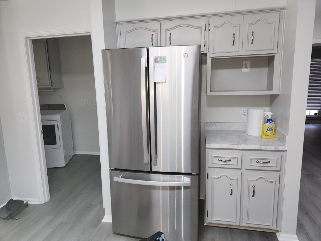 Modern kitchen renovation featuring stainless steel appliances, custom white cabinetry, and gray marble countertops installed by professional contractors.