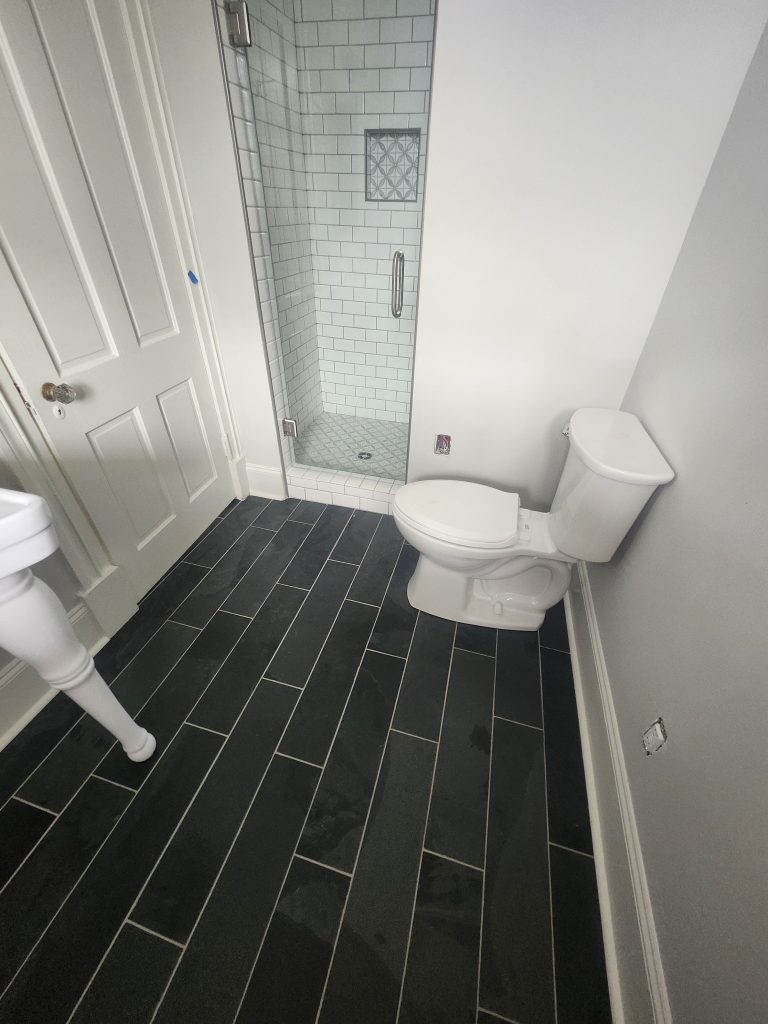 Professional bathroom renovation showcasing contrasting subway tile installation with gray-green and black tiles, modern fixtures, and quality painted finishes.
