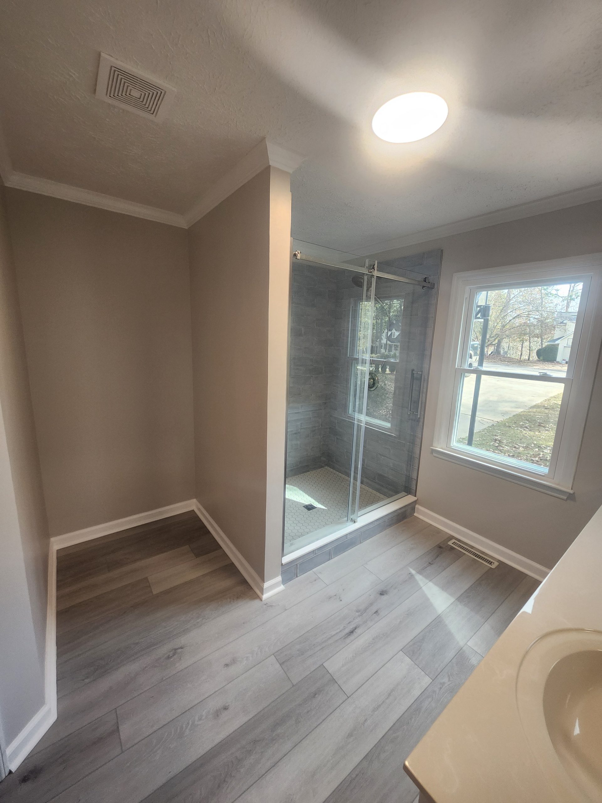 Modern bathroom renovation featuring soaking tub with glass enclosure, wood-look tile flooring, and skylight installation.