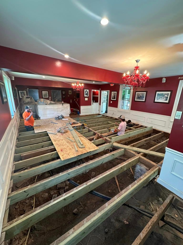 Professional flooring and structural renovation in progress with burgundy walls, white wainscoting, and exposed subflooring during comprehensive interior remodeling project.