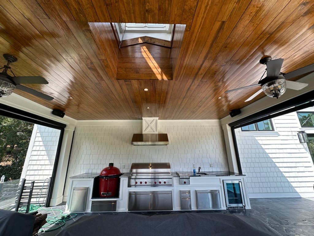 Modern outdoor kitchen pavilion with wooden plank ceiling, skylight, white shiplap walls, stainless steel appliances, and gas grill built by professional Aiken SC contractor.