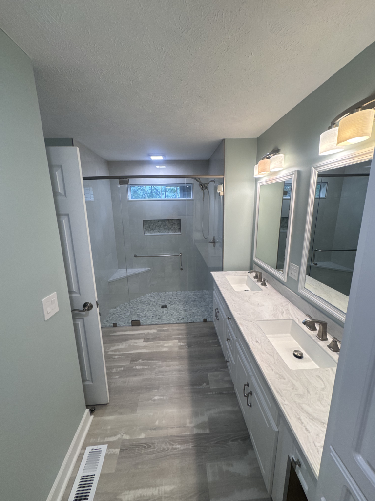 Luxury master bathroom renovation featuring marble countertops, double vanity, and frameless glass shower enclosure.