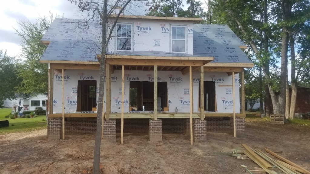 New residential construction with exposed framing, brick foundation, and Tyvek weather barrier installed by custom home builder in Aiken SC.