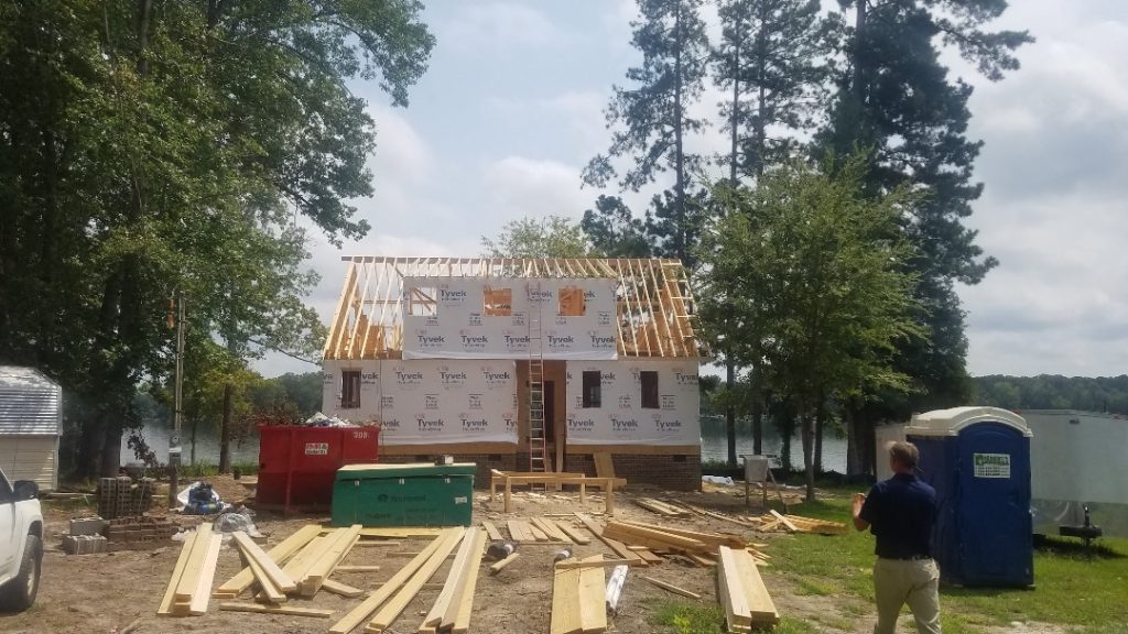 Residential home framing with exposed wooden trusses and Tyvek wrap during active construction on waterfront Aiken property.
