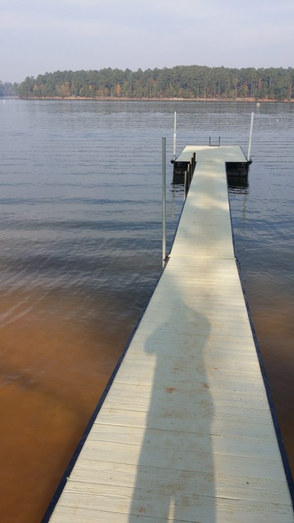 Pressure-treated wooden residential dock with white support posts extending into calm water, showcasing professional deck construction and materials.