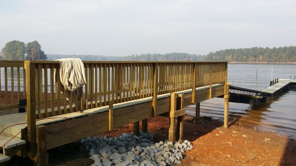 Professional deck builder constructing multi-section wooden dock with railings and floating sections along waterfront property in Aiken, SC.
