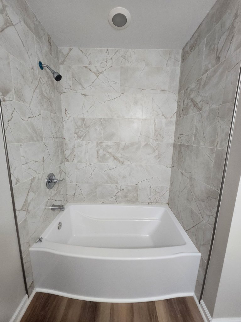 Modern bathroom renovation featuring curved soaking tub with marble-look tile surround and chrome fixtures in Aiken.