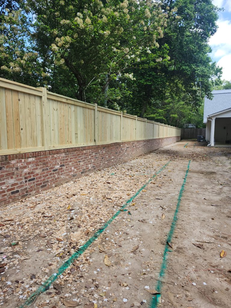 New brick and wood fence installation alongside driveway layout marked with chalk guides during residential construction project.