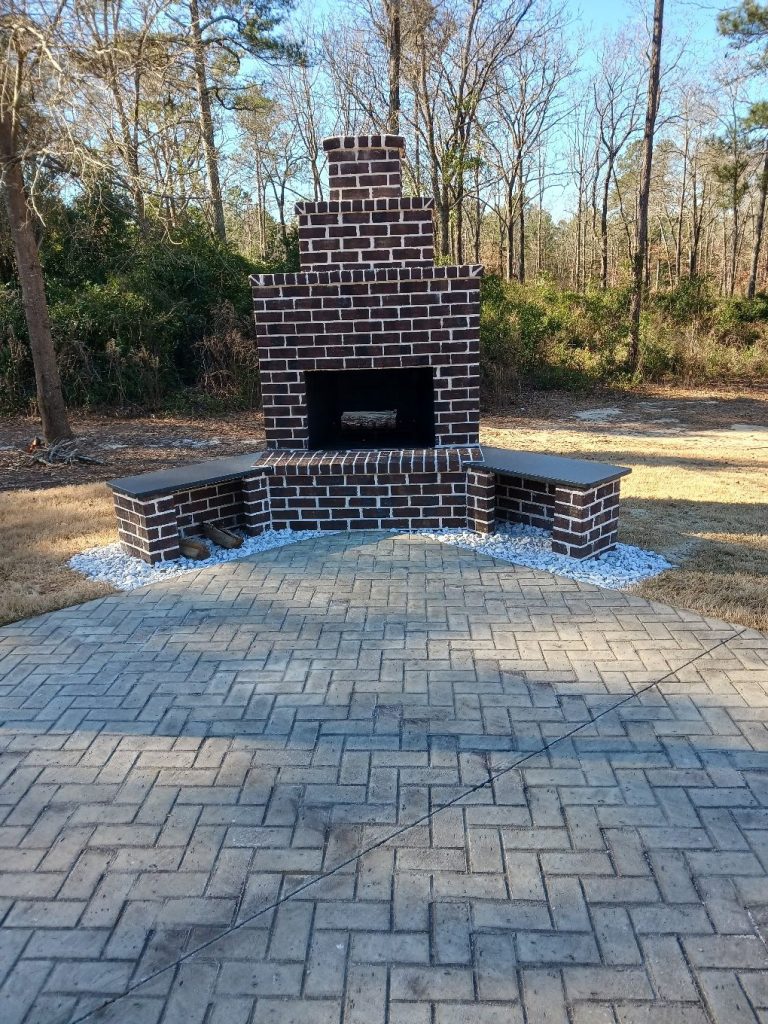 Custom brick fireplace with masonry chimney and paver patio, built-in seating, landscaping in wooded Aiken residential setting.