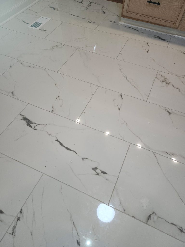 Professional installation of large-format porcelain tiles with marble veining in staggered plank pattern for modern kitchen flooring.